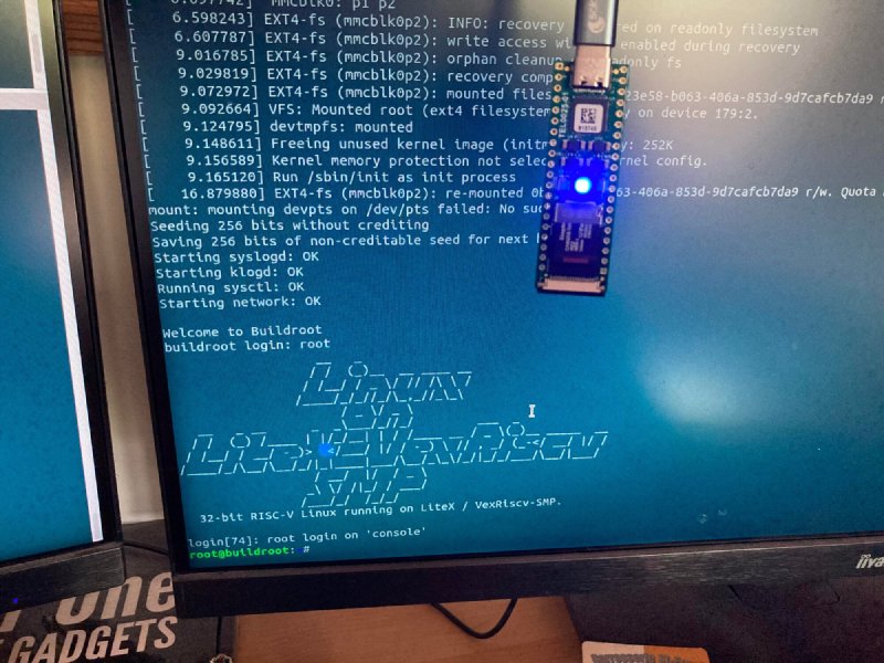 The DIPSY-40NX hanging in front of a monitor that shows its own serial console: EXT4 root mounted from mmcblk0p2, Buildroot login, the Linux on LiteX-VexRiscv SMP ASCII banner and a root shell